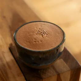 A warm cup of Mush Hut coffee blended with ceremonial cacao, served on a wooden block